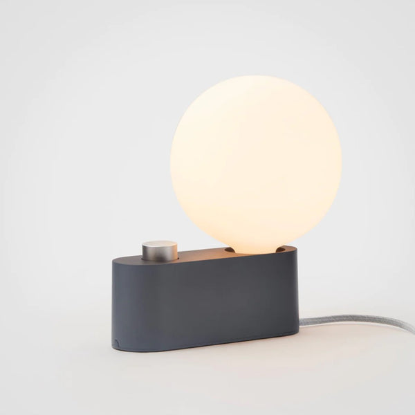 A modern table lamp with a matte-porcelain sphere-shaped shade and a charcoal black base, featuring a dimmable LED bulb, by Tala