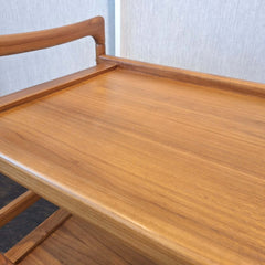 Close up of teak bar cart with two shelves on wheels and handles on both sides