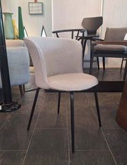 An off white fabric upholstered dining chair with a curved backrest and straight, conical metal legs.