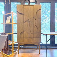 A simple bookcase with abstract patterns on the front doors, made of wood and finished in a new beech colour, with round brass door handles.