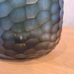 Fjord Vase 24cm in deep teal-blue frosted glass, its entire surface covered in dense small hammered cells that scatter light like sunlight breaking across cold, mineral-rich water.