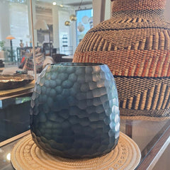 Fjord Vase 24cm in deep teal-blue frosted glass, its entire surface covered in dense small hammered cells that scatter light like sunlight breaking across cold, mineral-rich water.