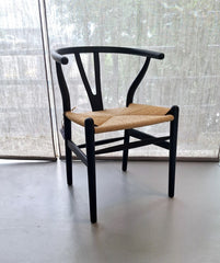 A black dining chair with a hard backrest and a natural finish rope seat.