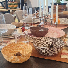 Table setting with Iraca woven straw bowls, glasses, and candles in a casual dining setting.