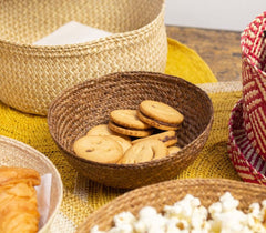 Handmade Iraca Small Bowl Plain Walnut baskets containing cookies, pastries, and popcorn on a yellow cloth.