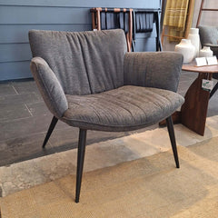 A black upholstered lounge chair with a relaxed design, featuring a flowing effect in the seating area and a hard backrest. The chair has black metal legs and is shown against a white background.