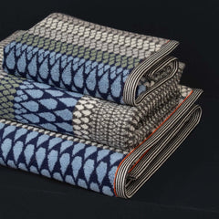 A family of blue grey patterned towels stacked, includes a Kensal Hand Towel, a bath towel and a bath sheet, by Margo Selby