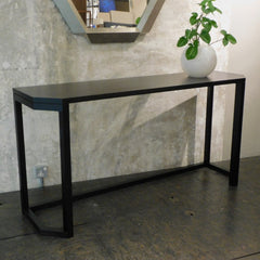 A black console table with angular front legs and a flat top, made of solid wood.