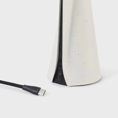 A portable lamp with a stone white finish, featuring a stainless steel structure and a Y-shaped LED light source.
