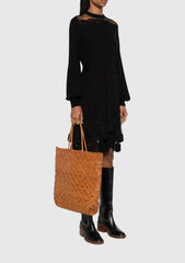 Woman wearing a black dress and tall boots, carrying the NS Corso Tan tote bag.