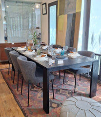 A rectangular charcoal-finished solid timber dining table with four asymmetrically positioned corner legs.
