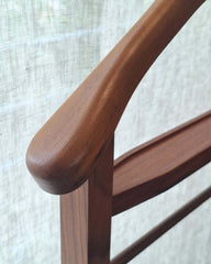 Close-up of a Ric Coat Hanger with a smooth, rounded endcap and a warm walnut finish, set against a light textured fabric background.