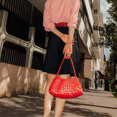 Person holding a Dragon Diffusion Rosanna Poppy Red woven leather handbag on a city street.
