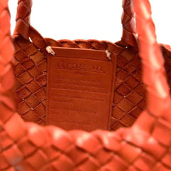 Close up of Dragon Diffusion Santa Croce Small Orange with asymmetric leather straps and a woven basket-like design. 