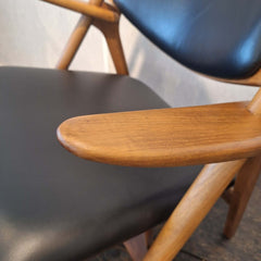 Close-up of a chair with Sawbuck Lounge Chair armrest and black leather seat and backrest.