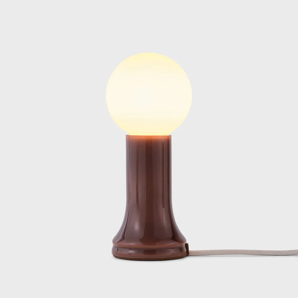 A table lamp with a mouth-blown bottle brown glass base and a matte white bulb, featuring an in-line dimmer, by Tala