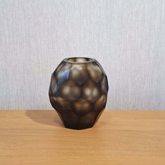 Sunhive Vase 16cm in warm smoky taupe frosted glass, its compact form wrapped in angular faceted cells that catch and hold the light with a quiet, burnished warmth.