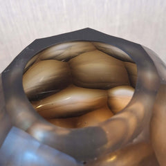 Sunhive Vase 16cm in warm smoky taupe frosted glass, its compact form wrapped in angular faceted cells that catch and hold the light with a quiet, burnished warmth.