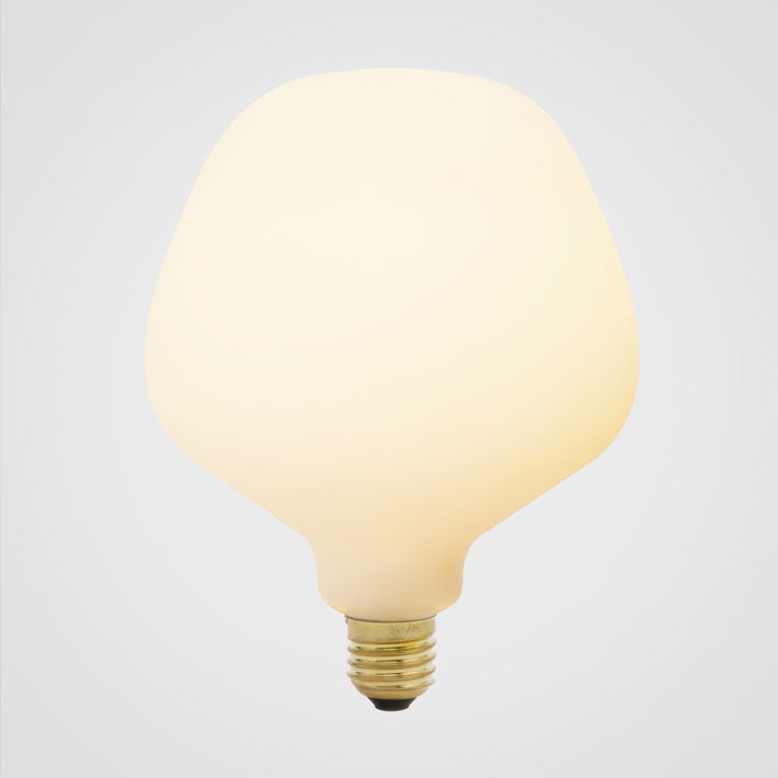 A trapezoid-shaped LED bulb with a matte glass finish, emitting a soft white light, designed to screw into an Edison-style base, by Tala