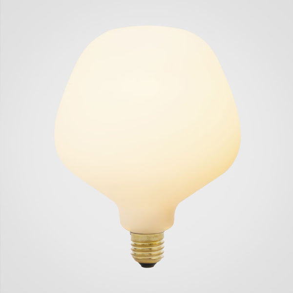 A trapezoid-shaped LED bulb with a matte glass finish, emitting a soft white light, designed to screw into an Edison-style base, by Tala