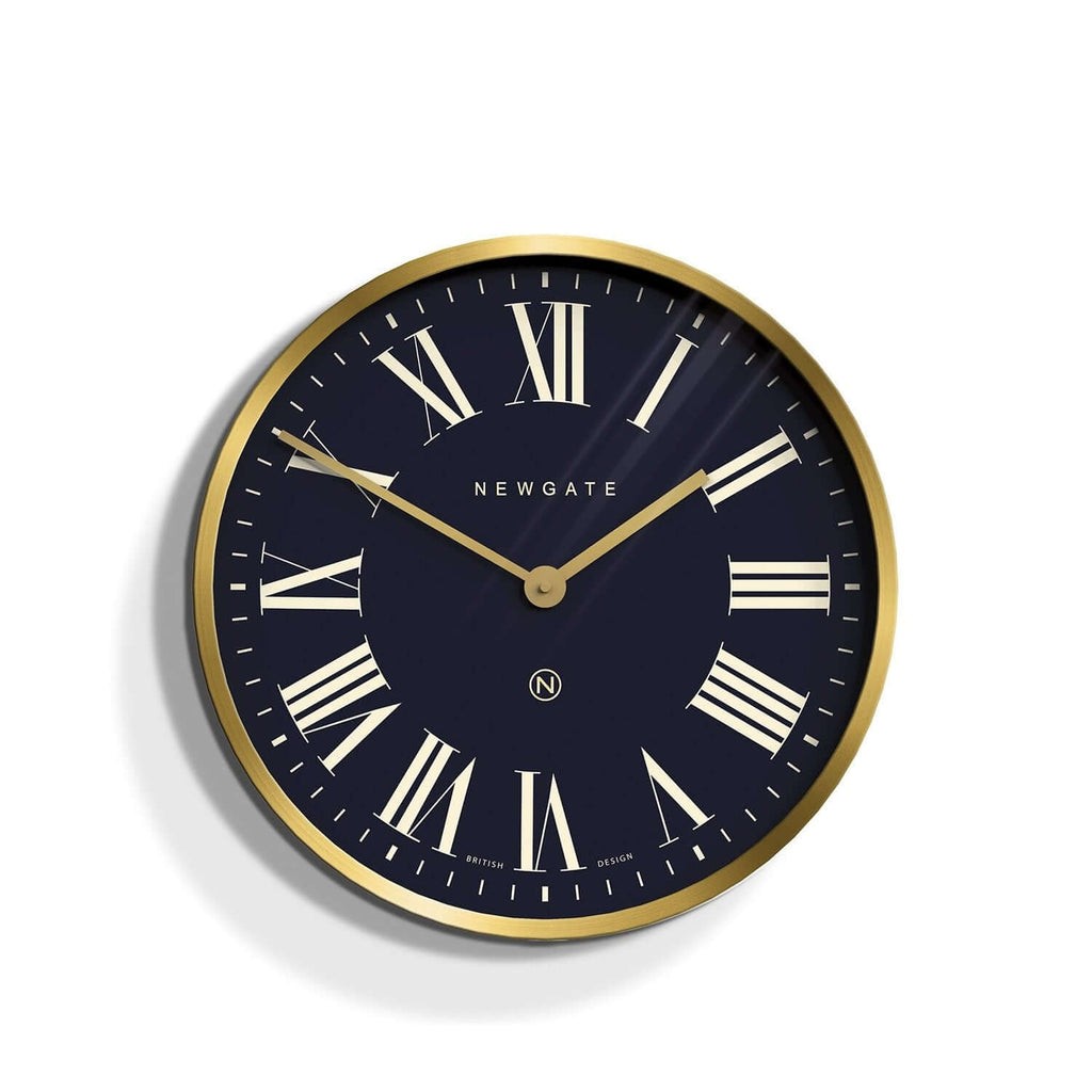 Newgate Mr Butler Wall Clock Brass with a black background, featuring Roman numerals and a matte brass case with a flat glass lens.
