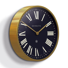 Newgate Mr Butler Wall Clock Brass with a black background, featuring Roman numerals and a matte brass case with a flat glass lens.