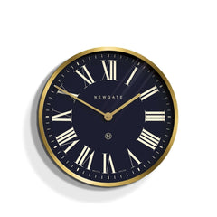 Newgate Mr Butler Wall Clock Brass with a black background, featuring Roman numerals and a matte brass case with a flat glass lens.