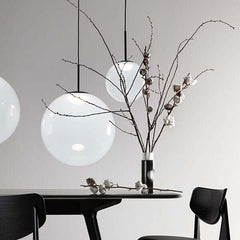 A white, spherical pendant light with a metallic suspension cable, emitting a soft glow, by Tom Dixon