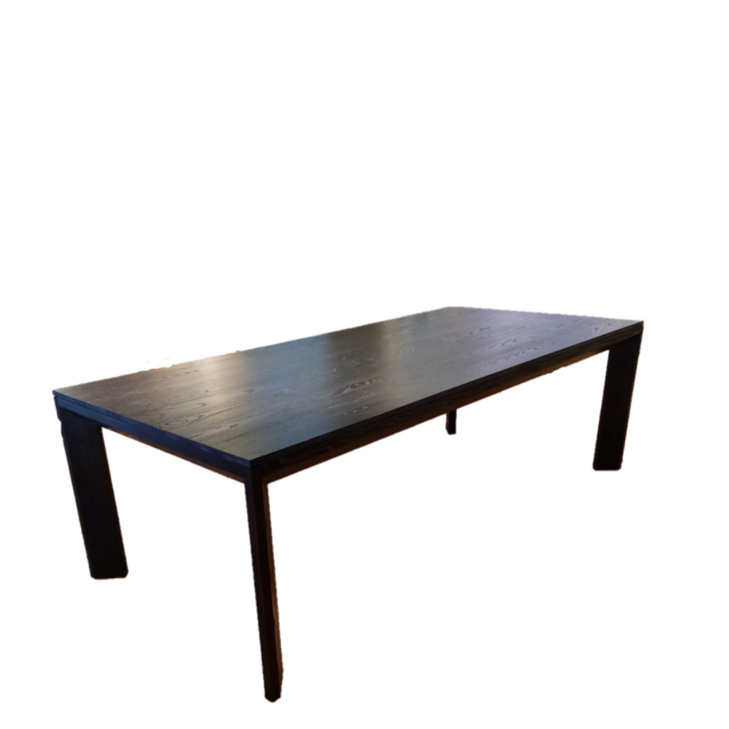 A modern rectangular dining table made of solid ash with a charcoal finish, featuring a mitre joint at the corners and stained legs.